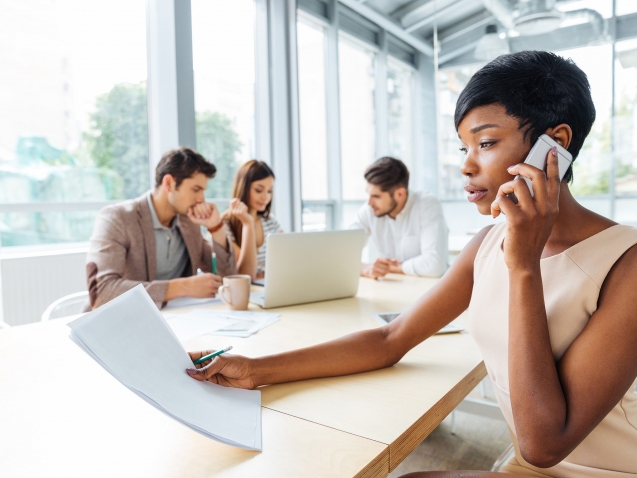 Serious businesswoman with documents talking on cell phone in office